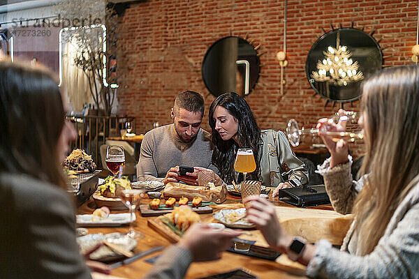 Frauen unterhalten sich beim Weintrinken mit Freunden und benutzen dabei ein Mobiltelefon im Hintergrund in einem Restaurant