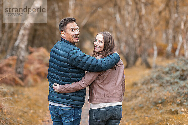 Lächelndes Paar  das im Herbst im Park steht und über die Schulter schaut