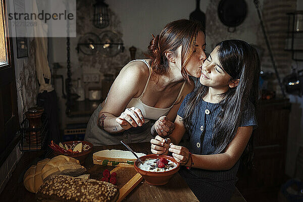 Mutter küsst Tochter  während sie in der Küche zu Hause steht