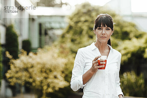 Selbstbewusste reife Geschäftsfrau  die eine Kaffeetasse hält  während sie vor Pflanzen steht