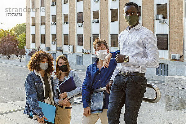 Universitätsstudenten tragen einen Gesichtsschutz  während sie auf der Treppe vor dem Bildungsgebäude stehen
