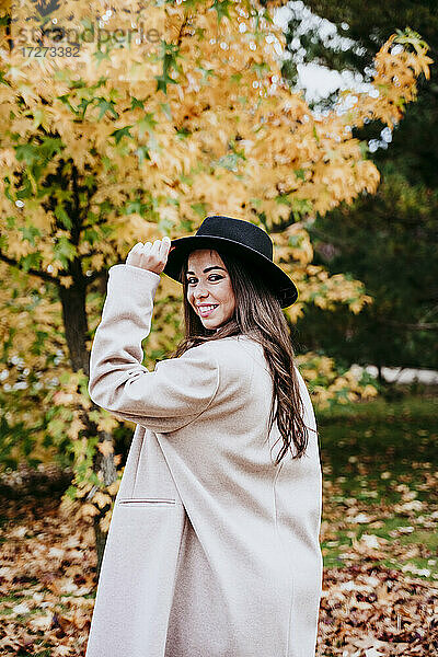 Schöne lächelnde Frau mit Hut  die vor einem Herbstbaum steht