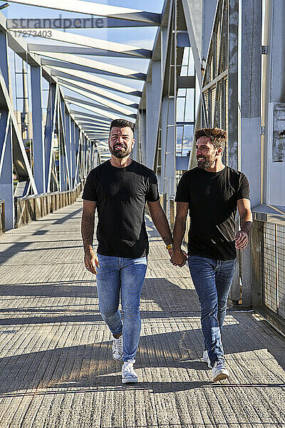 Glückliches homosexuelles Paar  das auf einer Brücke spazieren geht und dabei die Hände hält
