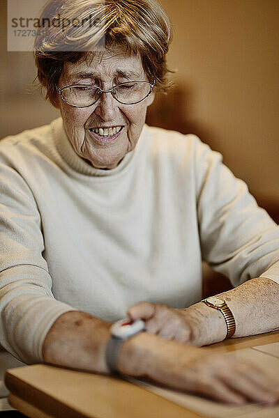 Runzlige Frau drückt Notrufknopf am Handgelenk über Tisch zu Hause