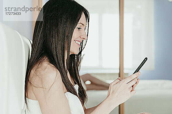 Lächelnde Frau mit Smartphone im Schlafzimmer zu Hause