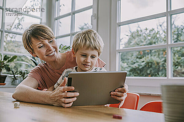 Mutter hält digitales Tablet mit Sohn  während sie zu Hause sitzt