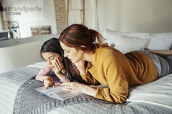 Mutter und Tochter lesen ein Buch  während sie zu Hause auf dem Bett liegen