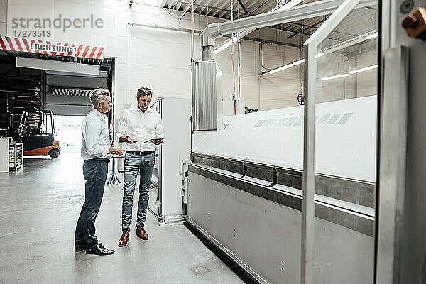 Männliche Ingenieure  die über ein digitales Tablet diskutieren  während sie an einer Maschine in der Industrie stehen