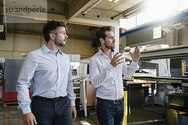 Junger Geschäftsmann schaut weg  während er mit einem Kollegen in einer modernen Fabrik diskutiert