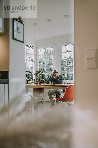 Depressiver Mann mit Kopf in den Händen sitzt zu Hause