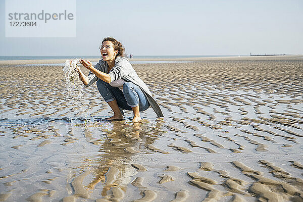 Fröhliche junge Frau spielt mit Wasser am Meer