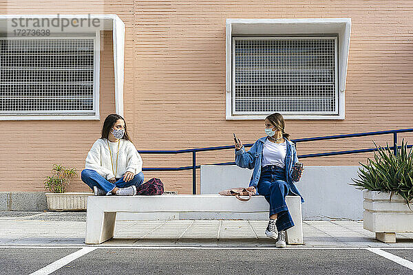 Freund fotografiert Teenager-Mädchen  das auf einer Betonbank sitzt