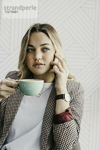 Junge Frau schaut weg  während sie in einem Café sitzt und Kaffee trinkt