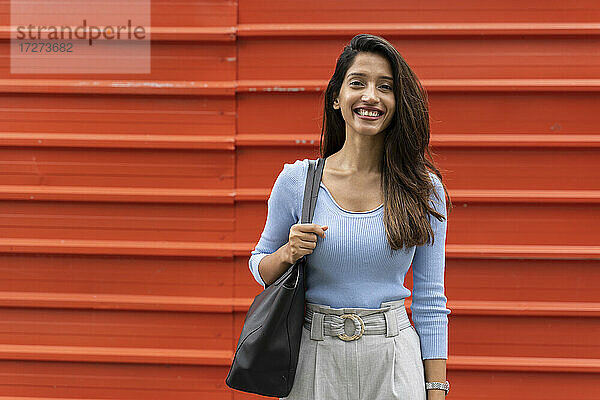 Lächelnde selbstbewusste Frau mit Handtasche  die vor einem Fensterladen steht