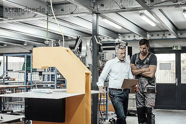 Männlicher Arbeiter und Manager diskutieren über ein Dokument  während sie in einer Fabrik stehen