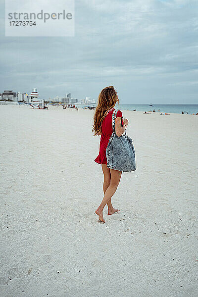 Junge Frau schaut auf das Meer  während sie auf dem Sand gegen den Himmel läuft