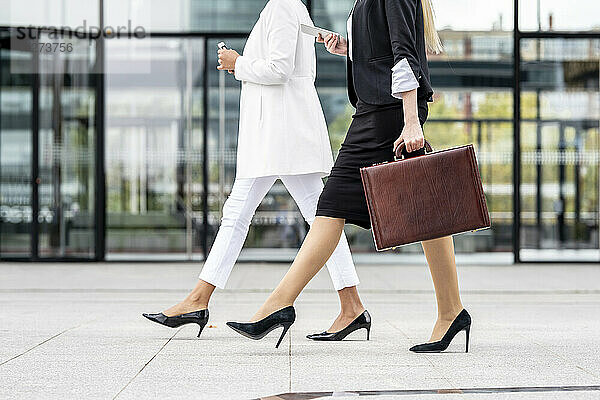 Geschäftsfrau mit Aktentasche  die ein Mobiltelefon benutzt  während sie an einem Kollegen auf dem Gehweg vorbeigeht