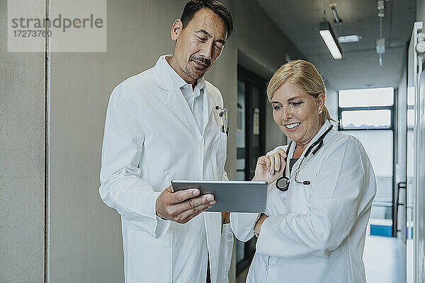 Lächelnder Wissenschaftler und Arzt  der ein digitales Tablet benutzt  während er im Klinikflur steht