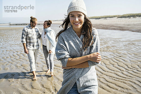 Lächelnde junge Frau beim Spaziergang mit Familie im Hintergrund am Strand