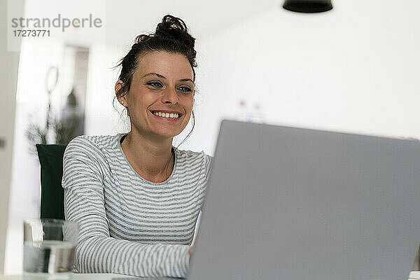 Lächelnde Frau  die zu Hause sitzend am Laptop arbeitet
