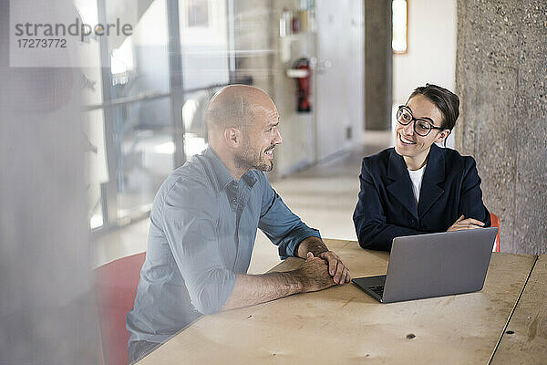 Lächelnde Geschäftsleute  die einen Laptop benutzen  während sie im Büro sitzen