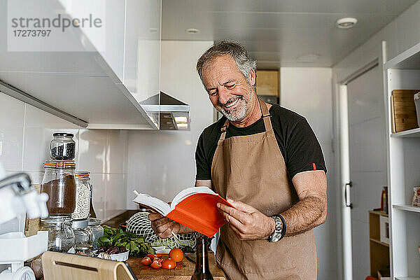 Älterer Mann lächelt beim Lesen eines Buches in der Küche zu Hause