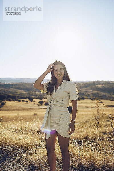 Lächelnde junge Frau steht auf einem Feld gegen den Himmel an einem sonnigen Tag