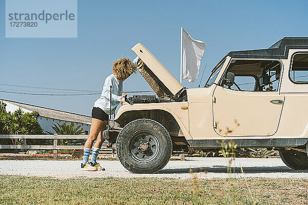 Junge Frau untersucht einen Geländewagen  während sie an einem sonnigen Tag mit offenem Verdeck steht