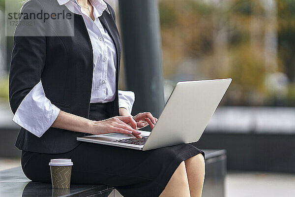 Geschäftsfrau  die einen Laptop benutzt und auf einer Bank im Freien sitzt