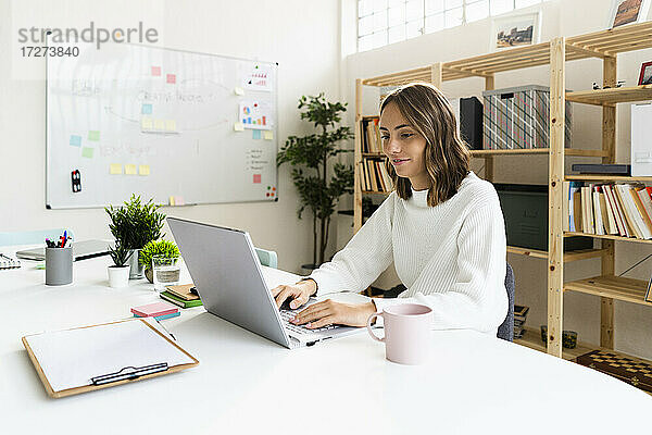 Geschäftsfrau arbeitet am Laptop  während sie am Tisch im Büro sitzt