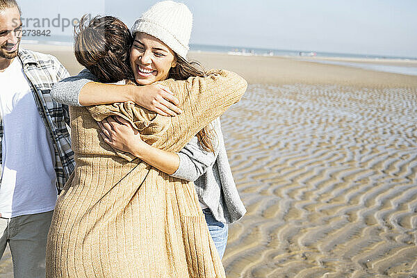 Mutter und Tochter umarmen sich  während sie neben einem Mann am Strand stehen