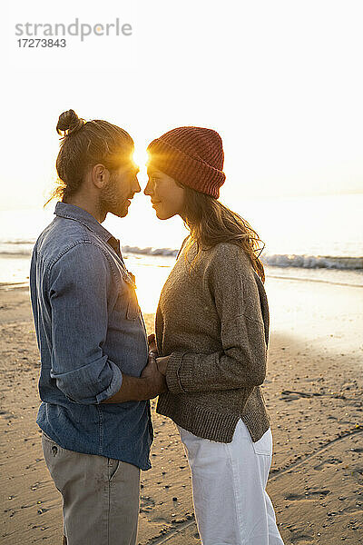 Romantisches junges Paar steht von Angesicht zu Angesicht am Strand bei Sonnenuntergang