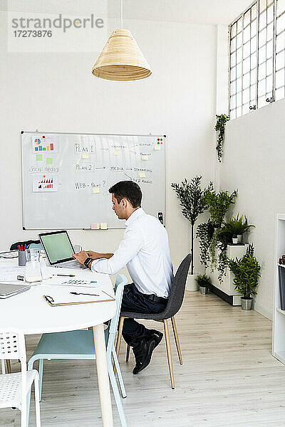 Männlicher Fachmann  der einen Laptop benutzt  während er am Schreibtisch sitzt und an einer Strategie im Büro arbeitet