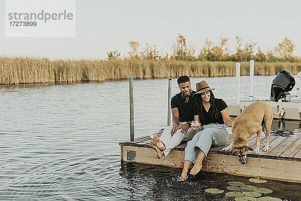 Lächelndes Paar mit Hund auf dem Pier sitzend