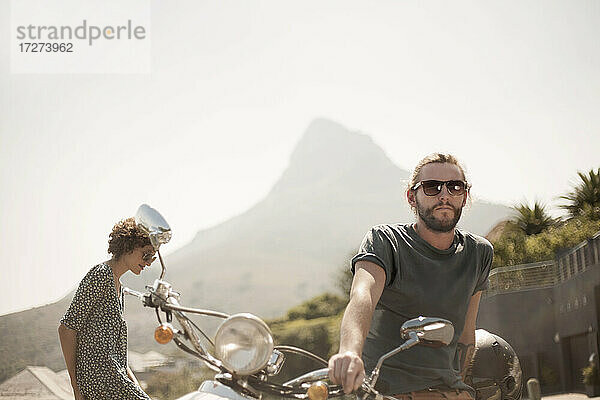 Mittlerer erwachsener Mann auf Motorrad sitzend mit Freundin an einem sonnigen Tag