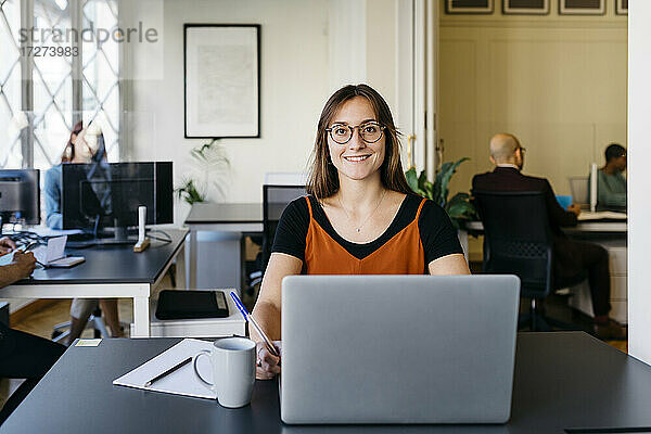 Lächelnde  zuversichtliche Geschäftsfrau bei der Arbeit am Bürotisch