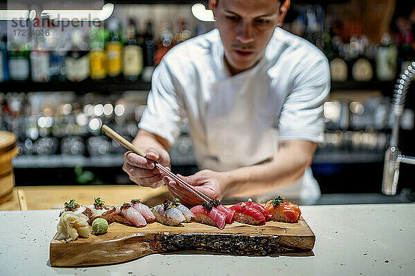 Männlicher Koch  der Sushi auf einem hölzernen Tablett in der Küche eines Restaurants garniert
