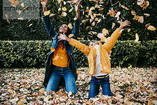 Lächelnde Mutter und Tochter spielen mit trockenen  gefallenen Blättern  während sie im Park knien