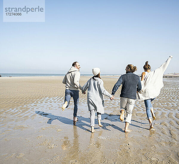 Verspielte Familie hält sich beim Laufen am Strand an den Händen