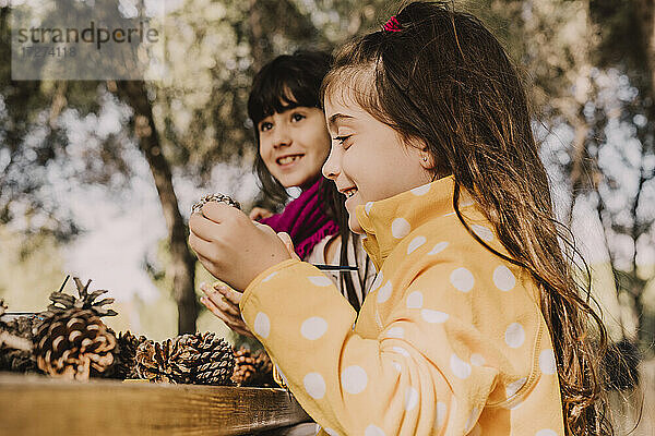 Lächelnd niedlichen Mädchen Färbung Tannenzapfen mit Schwester am Picknick-Tisch im Park
