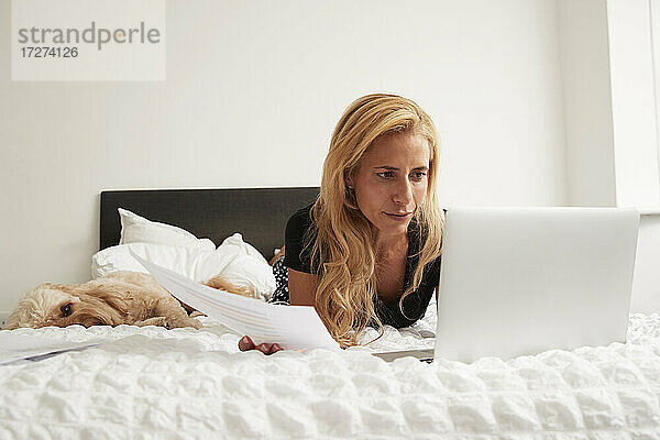 Reife Frau liegt auf der Vorderseite und benutzt einen Laptop zu Hause im Schlafzimmer