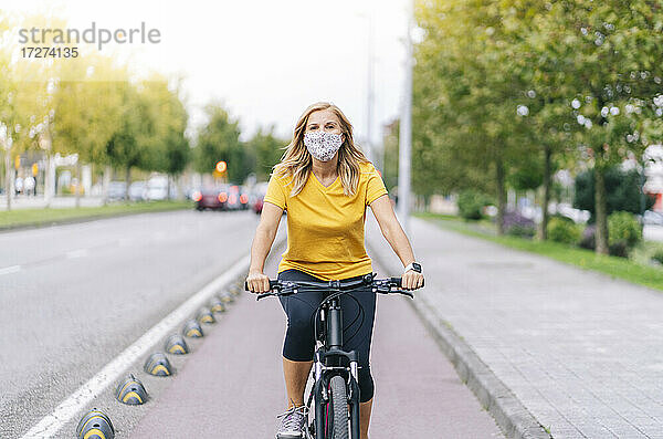 Frau mit Gesichtsschutzmaske beim Radfahren auf dem Radweg in der Stadt