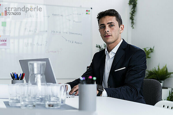 Selbstbewusster  gutaussehender Geschäftsmann sitzt mit Laptop am Schreibtisch in einem kreativen Arbeitsumfeld