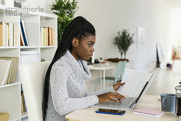 Studentin konzentriert sich beim Lesen einer Zeitung und studiert zu Hause am Laptop