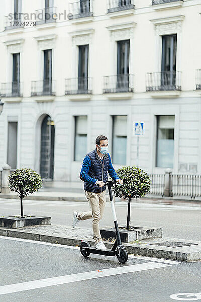 Junger Mann fährt während der COVID-19 mit einem elektrischen Roller auf einer Straße in der Stadt