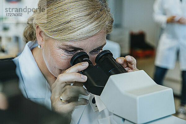 Wissenschaftlerin schaut durch ein Mikroskop  während ein Mann im Hintergrund im Labor steht