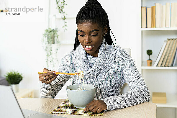 Junge Frau isst Nudeln  während sie zu Hause sitzt