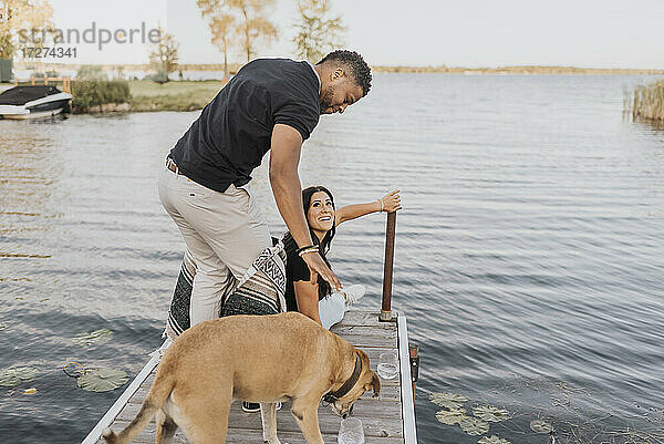 Mann steht mit Frau und Hund auf einem Steg am See