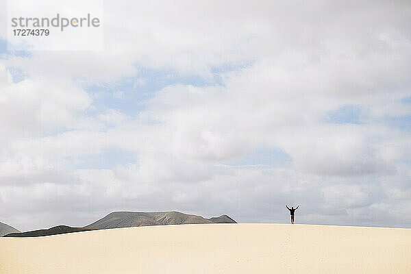 Mann steht am Sandstrand vor bewölktem Himmel