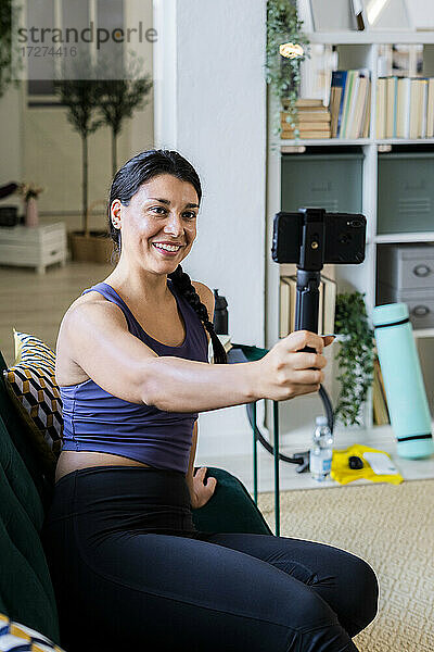 Weibliche Sportlerin  die zu Hause sitzend mit der Kamera aufnimmt